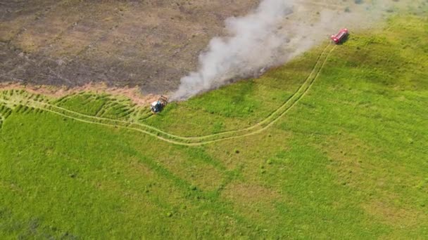 Vid kanten av branden på fältet, en traktor och en brandbil, rök virvlar — Stockvideo
