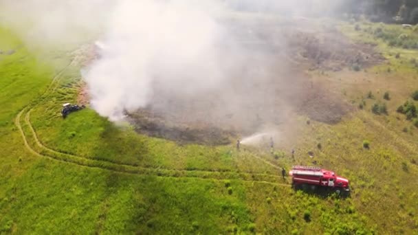 Aan de rand van het veld blussen een brandweerwagen en een brandweerman het vuur.. — Stockvideo