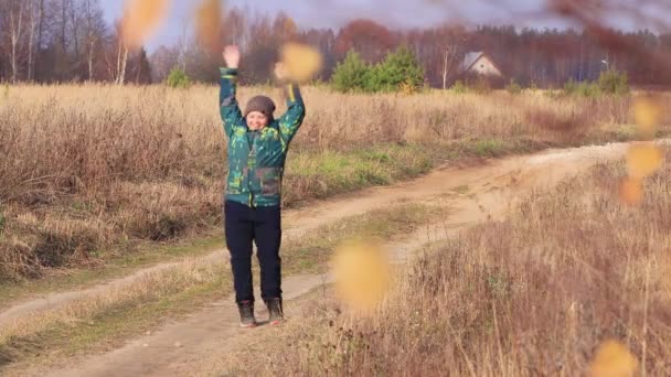 O menino está dançando, se divertindo e pulando em uma estrada rural no campo. — Vídeo de Stock