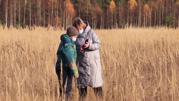 Mam en zoon met maskers op hun gezicht in het veld gebruik de telefoon — Stockvideo