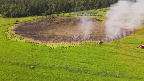 The burnt-out section of the field smokes, the tractor extinguishes the fire — 图库视频影像