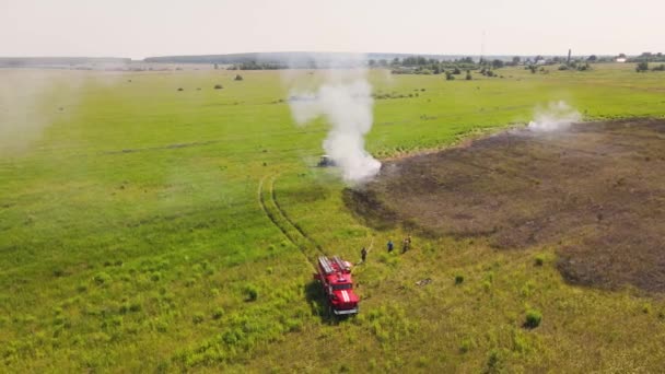 The edge of the burnt field is smoking, there is a fire engine and firefighters. — стоковое видео