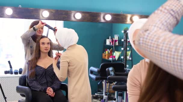 Uma menina é refletida no espelho, os mestres estilizam seu cabelo e pintam seus olhos — Vídeo de Stock