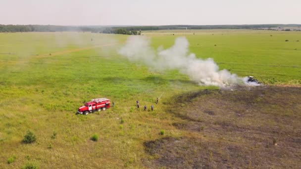 Aan de rand van een brandend veld, een brandweerauto en brandweerlieden. — Stockvideo