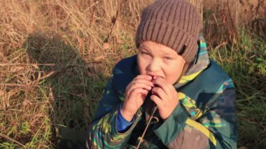 Uzun sarı çimenlerde oturan ve zevkle yemek yiyen bir çocuğun yakın çekimi..