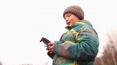 Gri gökyüzünün arka planında elinde telefon olan mutlu bir çocuk..