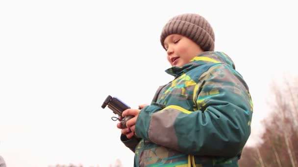 Στο φόντο του γκρίζου ουρανού, ένα χαρούμενο αγόρι με ένα τηλέφωνο στα χέρια του. — Αρχείο Βίντεο