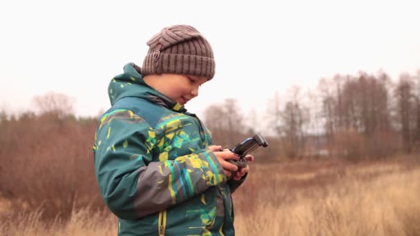 Lykkelig dreng med en telefon i hænderne griner, ser sig omkring. – Stock-video