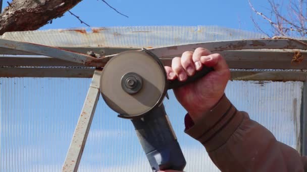 한 기술자 가손으로 비스듬 히 분쇄기로 녹슨 오래 된 금속 온실을 자르고 있다. — 비디오