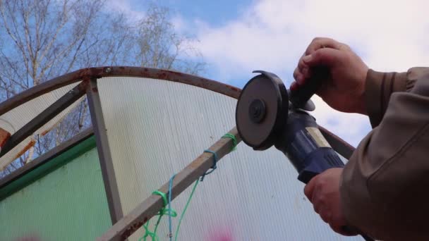 Hands with an angle grinder cut a rusty metal greenhouse. — Stock Video