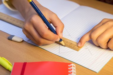 Bir öğrenci, cetvel boyunca bir kalemle deftere çizgi çizer..