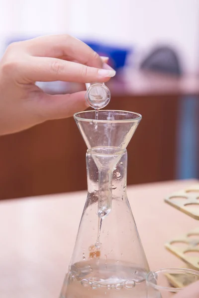 Close-up de um estudante mão derramando uma solução química em um frasco. — Fotografia de Stock