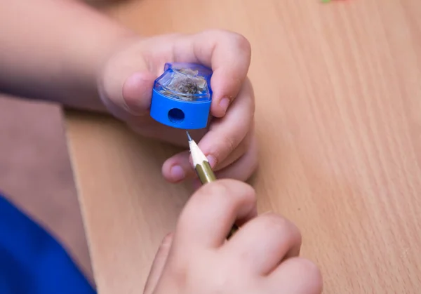 Close-up hands of a student insert a pencil into a sharpener.