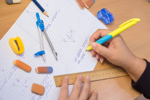 Pupils hand close-up solve a geometry example in a notebook.