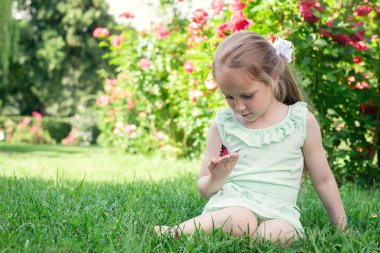 Küçük kız açık kelebek elinde tutar. 