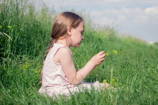 Meisje zittend In weide veld plukken bloemen — Stockfoto