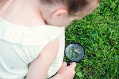 Çimlere bir büyüteç ile kız