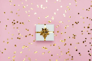 Pastel pembe arka planda altın fiyonklu beyaz hediye kutusu. Bayram kartı. Düz yatış, üst görünüm. 