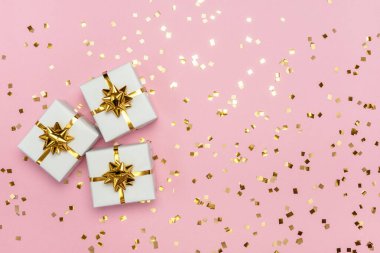 Pastel pembe arka planda altın fiyonklu beyaz hediye kutuları. Bayram kartı. Düz yatıyordu, boş alanı olan üst görünüm.  