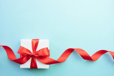 Mavi arka planda kırmızı kurdele yayı olan hediye kutusu. Noel, doğum günü ya da sevgililer günü hediyesi. Şenlikli dekor arka planı. Üst görünüm düz, boş alanı var.. 