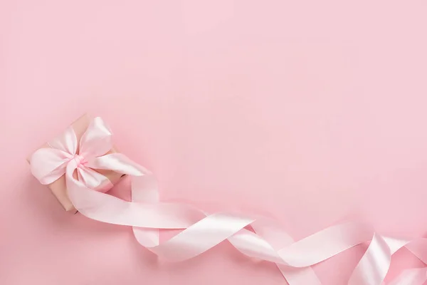 Pastel pembe arka planda uzun kurdeleli hediye kutusu. Sevgililer Günü, Anneler Günü ya da Kadınlar Günü hediyesi. Şenlikli tek renkli arka plan. Üst görünüm düz, boş alanı var..