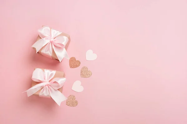 Pembe kurdeleli hediye kutuları ve pastel pembe arka planda kalpler. Sevgililer Günü kompozisyonu ve boş yer. Üst manzara, düz uzanma.