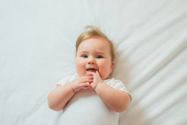 Beyaz çarşafların üzerinde uzanmış şirin bir bebek.