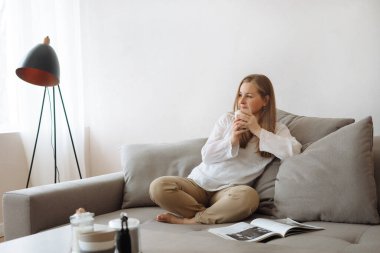 Evdeki sıcak içecekle kanepede dinlenen genç bir kadın..