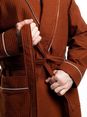 Parlak, banyo cüppeli bir adam beyaz bir arka planda kıyafet reklamları yapıyor. Stüdyoda yakın çekim..