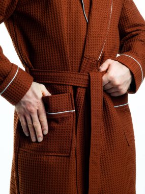 Parlak, banyo cüppeli bir adam beyaz bir arka planda kıyafet reklamları yapıyor. Stüdyoda yakın çekim..