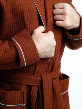 Parlak, banyo cüppeli bir adam beyaz bir arka planda kıyafet reklamları yapıyor. Stüdyoda yakın çekim..