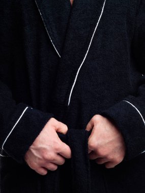 Parlak, banyo cüppeli bir adam beyaz bir arka planda kıyafet reklamları yapıyor. Stüdyoda yakın çekim..