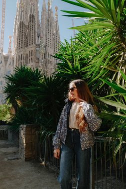 Genç bir kadın ayakta ve Sagrada Familia ile ejderha ağacının yanında gülümsüyor.