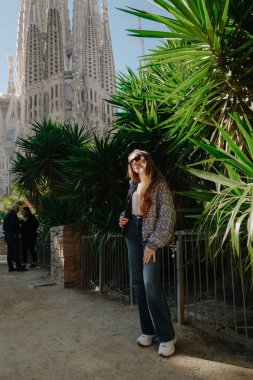 Genç bir kadın ayakta ve Sagrada Familia ile ejderha ağacının yanında gülümsüyor.