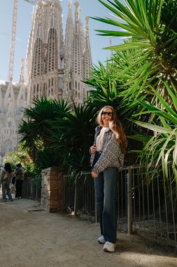 Genç bir kadın ayakta ve Sagrada Familia ile ejderha ağacının yanında gülümsüyor.