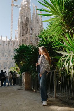 Genç bir kadın ayakta ve Sagrada Familia ile ejderha ağacının yanında gülümsüyor.