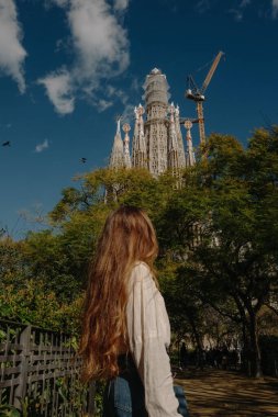 Kameraya arkası dönük genç bir kadın parkta Sagrada Familia 'ya bakıyor.