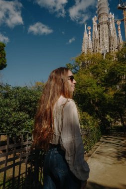 Kameraya arkası dönük genç bir kadın parkta Sagrada Familia 'ya bakıyor.