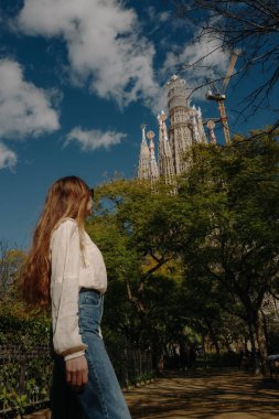 Kameraya arkası dönük genç bir kadın parkta Sagrada Familia 'ya bakıyor.