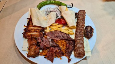 Çeşitli ızgara etler, patates kızartması ve tabakta ince pide ekmeği..