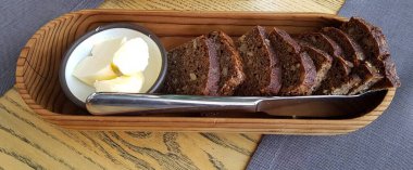 Dilimlenmiş çavdar ekmeği ve rosette tereyağı ahşap tepside servis edilir..