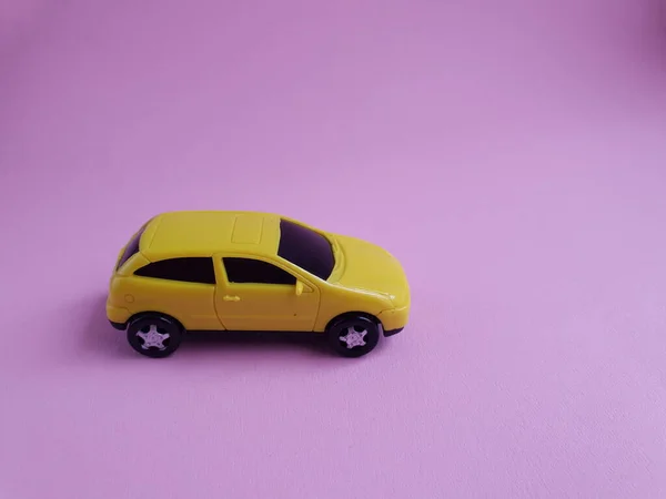 yellow toy car on a pink background, a concept idea of a taxi and delivery of goods during quarantine.