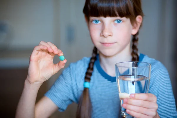 Capsules, pills in one hand, a glass of water in the other. The girl is holding the medicine in front of her. Close-up.