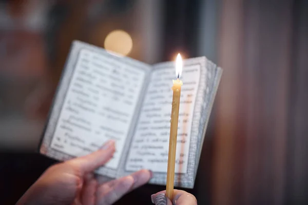 candle in hand and a book of prayers close-up in the Orthodox Church