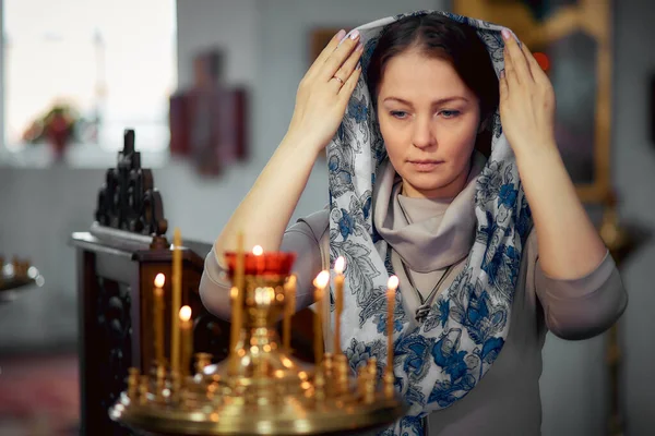 lifestyle woman lights candles in the Church, praying in front of the icon