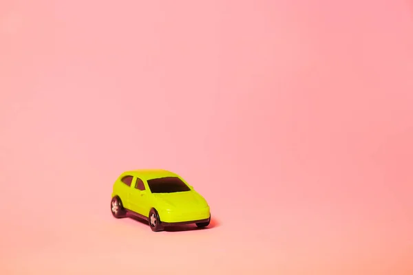 yellow toy car on pink background, concept idea of taxi and cargo delivery during quarantine.