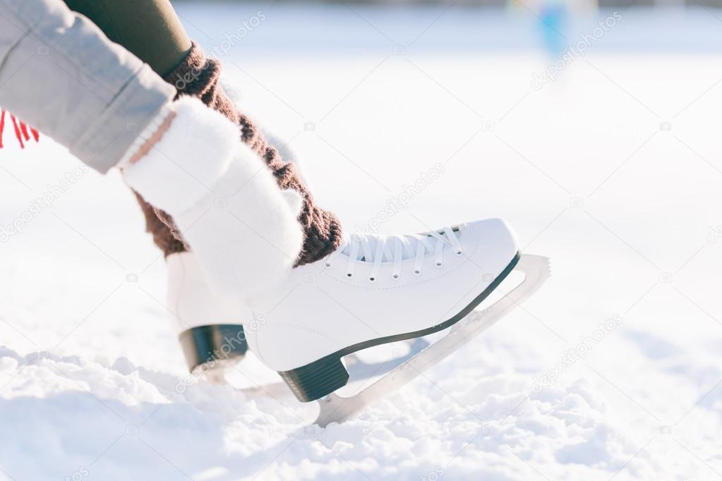Girl in dress skates mittens tying shoelaces