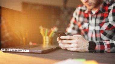 genç adam akıllı telefon ve dizüstü bilgisayar kullanarak evden çalışma.