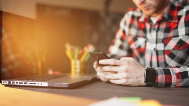 Joven que trabaja desde casa usando el teléfono inteligente y la computadora portátil . — Vídeos de Stock