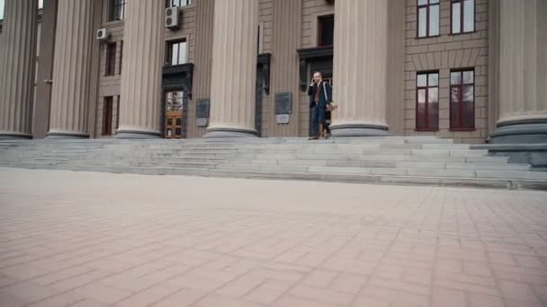 Estudiante dejando la universidad sosteniendo sus libros de texto y mochila — Vídeos de Stock